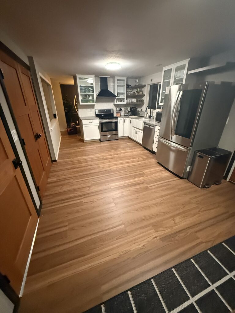 Kitchen remodel in Eugene, Oregon featuring white cabinets, stainless steel appliances, wood-look flooring, open shelving, and a black range hood.