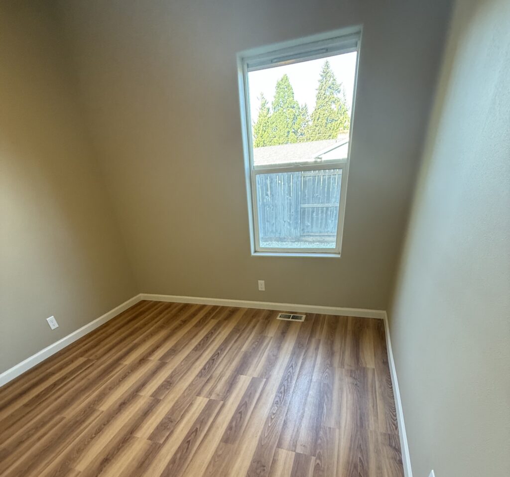 Interior painting in Springfield, Oregon with neutral walls, white baseboards, a large window, and wood-look flooring.