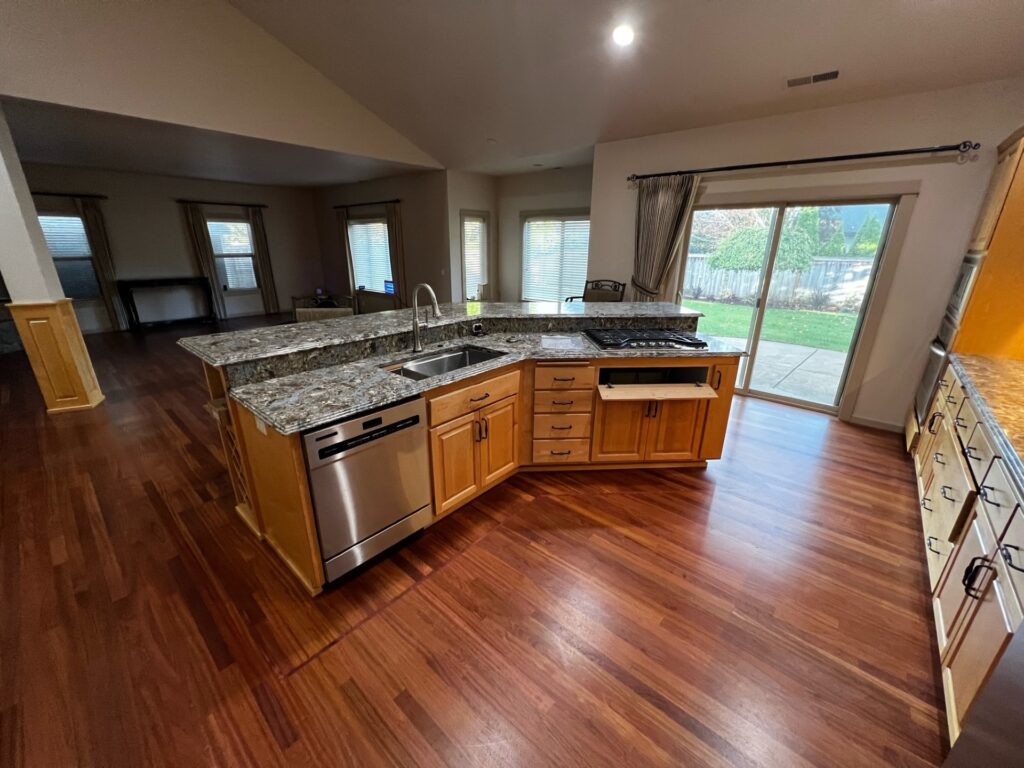 Kitchen remodel in Junction City, Oregon featuring wood cabinets, stone countertops, stainless steel appliances, hardwood flooring, island and an open kitchen layout.