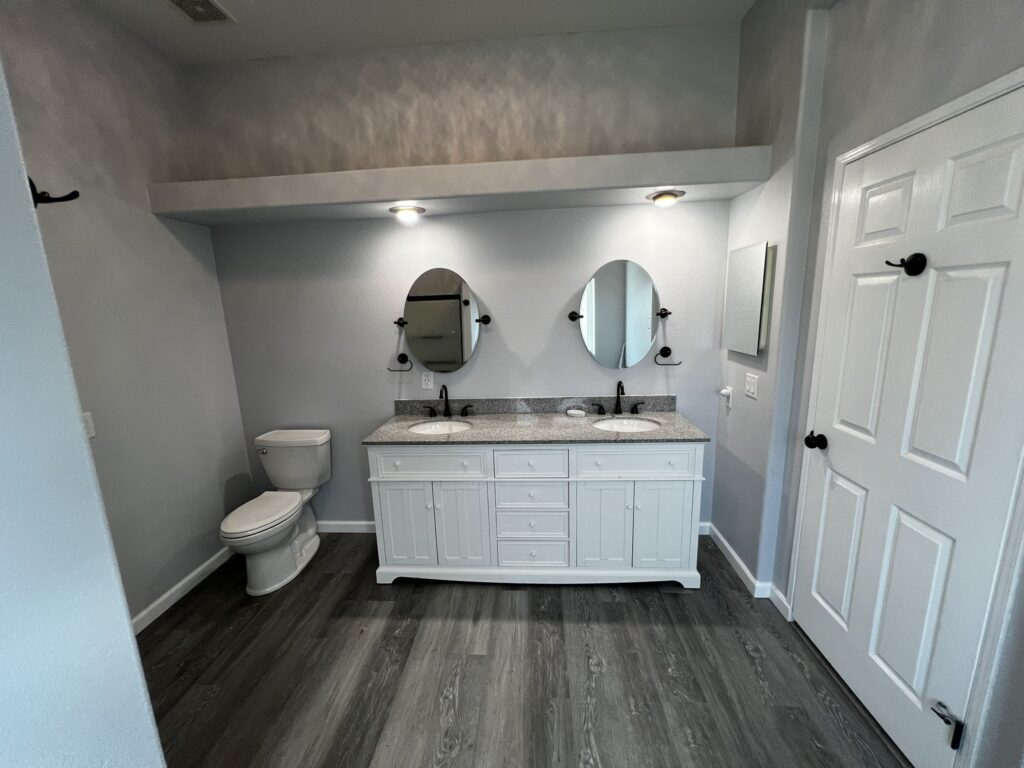 Bathroom remodel with new double vanity, LED lighting, and grey wood luxury vinyl plank in Veneta, Oregon. 